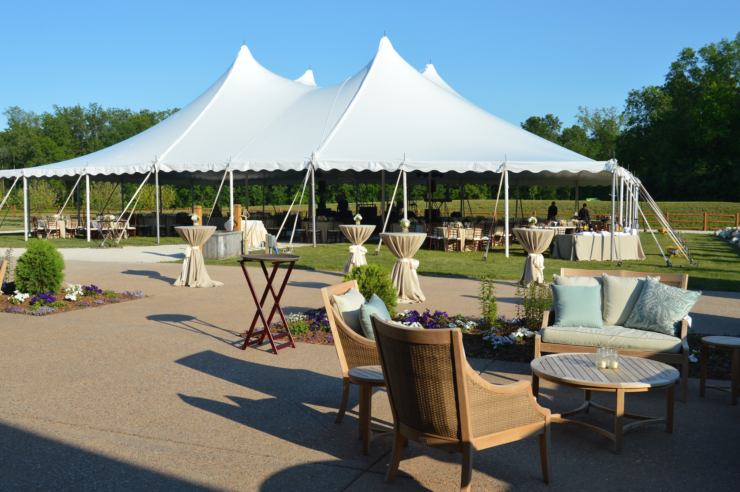 The Lawn set up with outdoor furniture with teal and beige colors, along with a tent that is set up with tables and chairs under it.