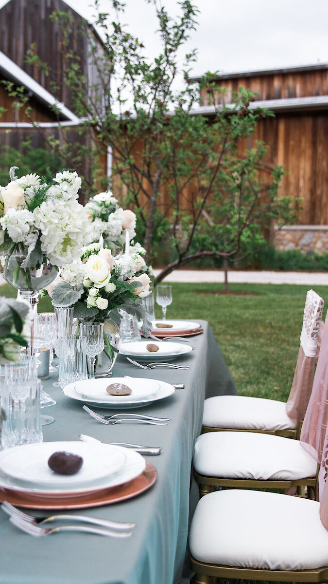 A vintage inspired table with teal and pink accents is set with vintage crystal in preparation for a wedding reception. 