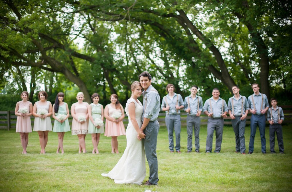A wedding party photographed in the Meadow with the bride and groom close together in the foreground and the party slightly blurry in the back. 