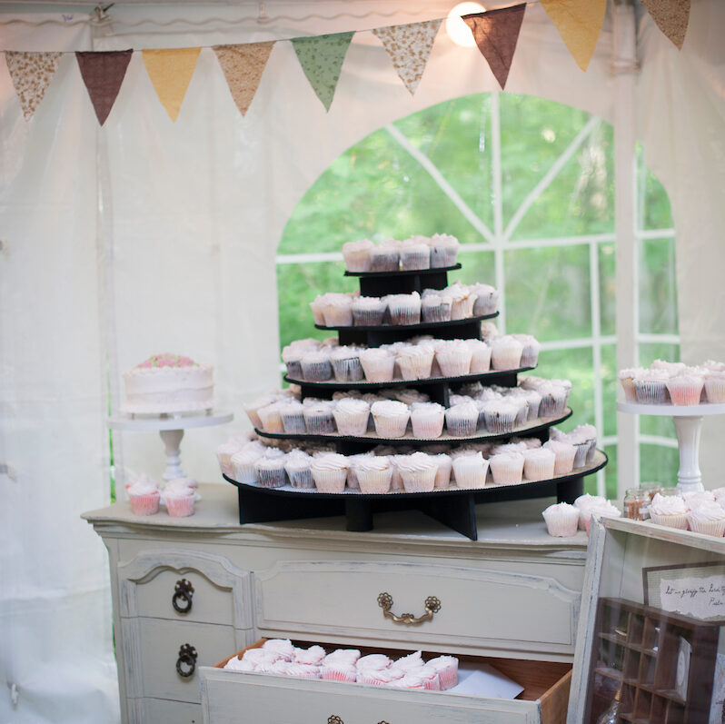A cupcake tower in a tent on a vintage white dresser in the reception of this wedding