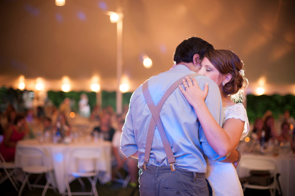 A couple embrace on the dance floor at night under a tent at a Lawn wedding