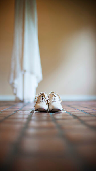 Vintage oxford white shoes in the foreground and a dress hanging from the chandelier in the Bridal dressing room in Interpretation building